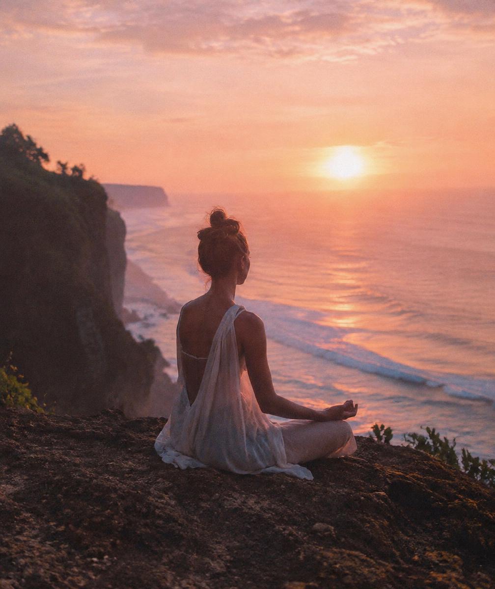 Woman meditating on a cliff above the ocean at sunrise